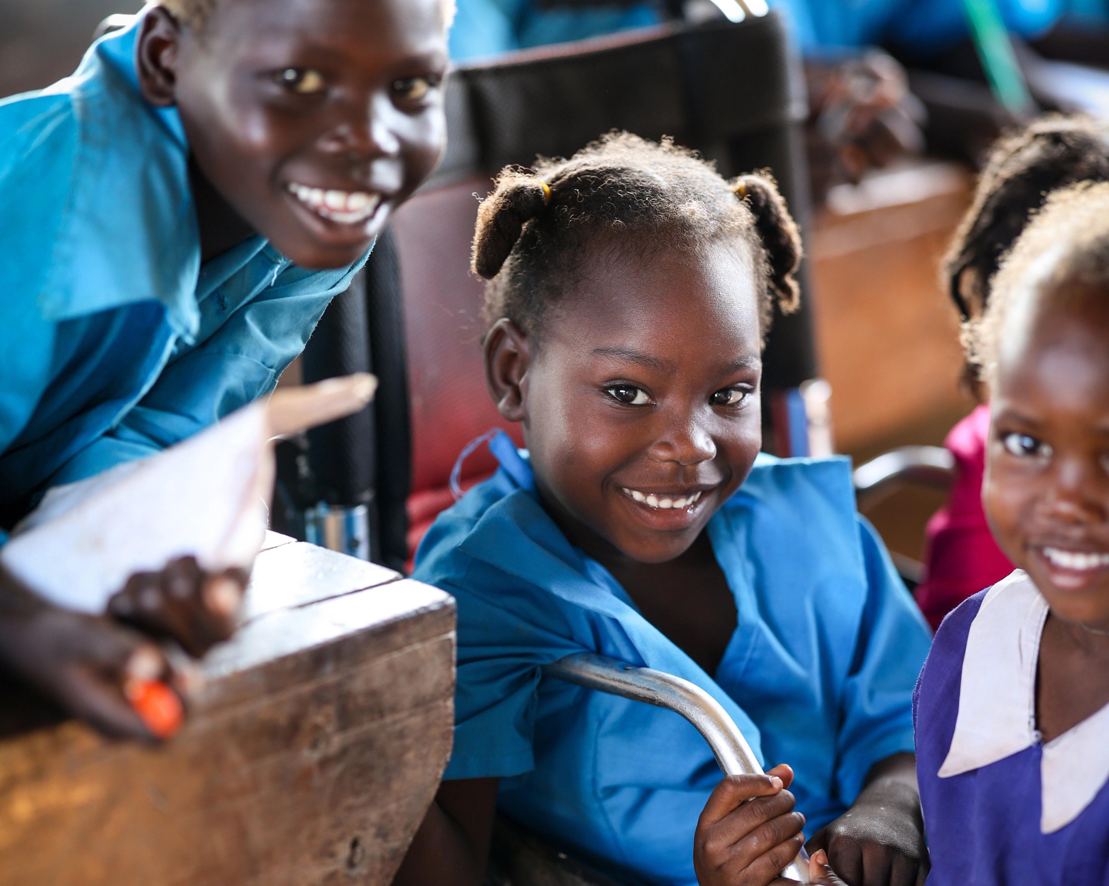 Tre glada barn, flickan i mitten sitter i en enkel rullstol